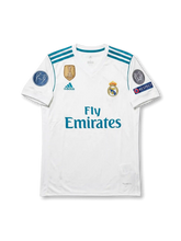 Front view of Real Madrid 2017-18 Champions League home shirt with white body, teal detailing, Fly Emirates sponsor, club crest, and European sleeve patches.