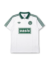 Front view of Adidas Originals x Oasis Live ’25 special edition polo shirt with white body, green stripes, trefoil logo, circular crest detail, and Oasis front branding.