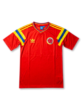 Front view of Colombia 1990 away shirt with red body, yellow and blue shoulder stripes, V-neck collar, and Colombia crest.