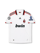 Front view of AC Milan 2009-10 away shirt with white body, red-and-black trim, bwin sponsor, club crest, and Champions League sleeve patches.