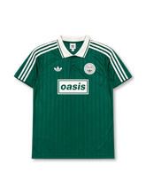 Front view of Oasis × adidas Originals Live ’25 green jersey with white polo collar, tonal vertical stripes, Oasis chest graphic, trefoil logo, and Live ’25 crest detail.