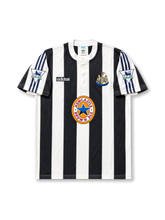 Front view of Newcastle United 1995-97 home shirt with black-and-white stripes, Newcastle Brown Ale sponsor, club crest, buttoned collar, and Premier League sleeve patches.