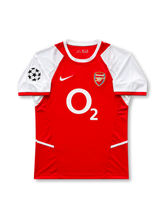 Front view of Arsenal 2002-04 home shirt with red body, white sleeves, O2 sponsor, Arsenal crest, and UEFA Champions League sleeve patch.