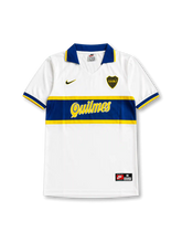 Front view of Boca Juniors 1996-97 away shirt with white body, blue and yellow chest band, Quilmes sponsor, Boca Juniors crest, and blue collar.