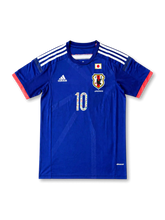 Front view of Japan 2014 Captain Tsubasa home shirt with blue body, Japan crest, national flag detail, #10 manga-style chest number, and coral sleeve trim.