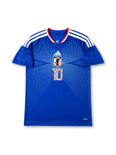 Front view of Japan 2006 Captain Tsubasa home shirt with blue body, Japan crest, white line graphics, #10 manga-style chest number, and red collar trim.