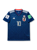 Front view of Japan 2018 Captain Tsubasa home shirt with blue pinstripe body, Japan crest, #10 illustrated number, white shoulder stripes, and FIFA sleeve patches.