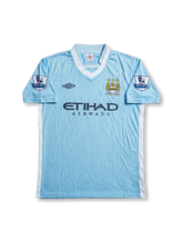 Front view of Manchester City 2011-12 home jersey with sky blue body, Etihad Airways sponsor, club crest, and Barclays sleeve patches.