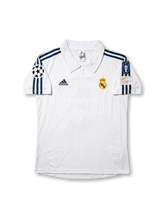 Front view of Real Madrid 1998-00 home shirt with white base, club crest, dark navy shoulder stripes, and Champions League sleeve patch.