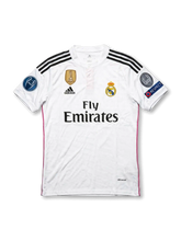 Front view of Real Madrid 2014-15 home shirt with white base, club crest, Fly Emirates sponsor, FIFA World Champions badge, and Champions League sleeve patches.