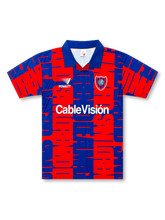 Front view of San Lorenzo 1990s graphic shirt with red and blue all-over pattern, club crest, Penalty logo, CableVisión sponsor, and blue fold collar.
