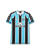 Front view of Grêmio 2000 home shirt with black, sky blue, and white vertical stripes, club crest, Astra sponsor, Chevrolet logo, and white fold collar.