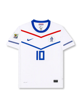 Front view of Netherlands 2010 World Cup away shirt with white base, blue collar, red and blue chevron graphics, KNVB crest, central #10 print, and South Africa 2010 sleeve patch.
