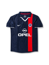 Front view of Paris Saint-Germain 2001-02 home shirt with navy base, red vertical center stripe, PSG crest, Opel sponsor, white collar detail, and short sleeves.