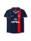 Front view of Paris Saint-Germain 2001-02 home shirt with navy base, red vertical center stripe, PSG crest, Opel sponsor, white collar detail, and short sleeves.