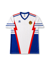 front view of Yugoslavia 1998 World Cup away shirt with white base, blue side panels, red geometric details, adidas trefoil logo, and national crest