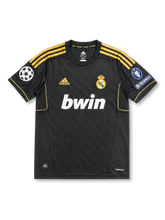 front view of Real Madrid 2011-12 away shirt with black body, gold adidas stripes, bwin sponsor, Real Madrid crest, Champions League patch, and UEFA Respect patch