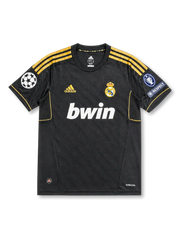 front view of Real Madrid 2011-12 away shirt with black body, gold adidas stripes, bwin sponsor, Real Madrid crest, Champions League patch, and UEFA Respect patch