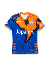 front view of V-Varen Nagasaki 2018 home shirt with blue and orange graphic design, V-neck collar, Hummel logo, club crest, Japanet sponsor, J.League sleeve patch, orange chevron accents, wave lines, and bird graphic details