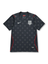 USA 2026/27 away shirt with a dark charcoal base, tonal all-over star pattern, white USA shield crest, white chest Swoosh, red piping accents, and V-neck collar.