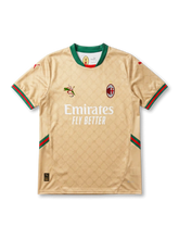 Front view of AC Milan special edition shirt in gold with monogram pattern, Emirates Fly Better sponsor, green collar, and red-green trim accents.