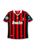 Front view of AC Milan home shirt in red and black stripes with white collar, bwin sponsor, adidas logo, club crest, and European competition sleeve patches.