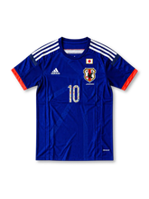 サッカー日本代表 2014年ホームユニフォーム キャプテン翼 大空翼10番モデル adidas製ジャパンブルーのボディにホワイトのスリーストライプス、蛍光コーラルレッドの袖口と背面ライン、JFA八咫烏エンブレムと日本国旗、漫画イラスト入りの背番号10、背面のTSUBASAネームを配したレトロサッカージャージ