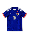 日本代表 2018年 ホームユニフォーム キャプテン翼10番 スペシャルエディション。濃いジャパンブルーのボディに刺し子風の縦ライン柄、ホワイトの肩のスリーストライプ、レッドの縁取りを施したVネックを組み合わせ、胸元に日本国旗、JFAエンブレム、adidasロゴ、キャプテン翼の漫画イラスト入り10番を配したサッカージャージ。両袖にはキャプテン翼とLiving Football FIFAのデザインパッチをあしらった特別仕様。