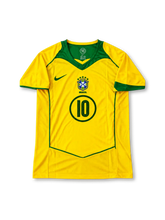ブラジル代表 2004年 ホームユニフォーム ロナウジーニョ10番。Nike製の鮮やかなカナリアイエローのボディにグリーンのVネックと肩から脇にかけての切り替え、曲線状のパイピングを施し、胸元にグリーンのNikeロゴ、5つ星付きCBFエンブレム、円形フレーム入りの10番を配したレトロサッカージャージ。背面にはRONALDINHOのネームとグリーンの10番をあしらったデザイン。