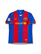 FCバルセロナ 2007/08シーズン ホームユニフォーム リオネル・メッシ19番。Nike製のブルーとエンジの太い縦ストライプに、ブルーのVネックとゴールドの袖口ラインを組み合わせたレトロサッカージャージ。胸元にはイエローのNikeロゴ、UNICEFロゴ、カンプ・ノウ開場50周年を記念した月桂樹と1957–2007の文字入りクラブエンブレムを配置。袖にLFPパッチを備え、背面にはMESSIのネームとイエローの19番、襟下にカタルーニャ旗を配したデザイン。