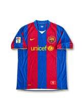 FCバルセロナ 2006/07シーズン ホームユニフォーム ロナウジーニョ10番。Nike製のブルーとエンジの太い縦ストライプにレッドのVネックを組み合わせ、胸元にはイエローのNikeロゴ、UNICEFロゴ、カンプ・ノウ開場50周年を記念した1957–2007の文字入りクラブエンブレムを配置したレトロサッカージャージ。袖にはLFPパッチを備え、背面にはRONALDINHOのネームとイエローの10番を配したデザイン。
