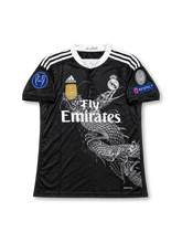 レアル・マドリード 2014/15シーズン サードユニフォーム クリスティアーノ・ロナウド7番。adidasと山本耀司によるデザインで、ブラックのボディにダークグレーの龍と鳳凰のグラフィックを大胆に配し、ホワイトのスタンドカラーと肩のスリーストライプを組み合わせたレトロサッカージャージ。胸元にはホワイトのadidasロゴ、モノトーンのクラブエンブレム、Fly Emiratesスポンサーロゴを配置。袖にはUEFAチャンピオンズリーグのパッチ、RESPECTパッチ、10回優勝を示す記念バッジを備え、背面にはRONALDOのネームとホワイトの7番を配したデザイン。