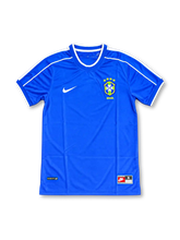 ブラジル代表 1990年代 ブルーアウェイユニフォーム。Nike製の鮮やかなロイヤルブルーのボディに、肩から袖にかけて走るホワイトのパイピングとホワイトの袖口ラインを組み合わせたレトロサッカージャージ。胸元にはNikeのスウッシュロゴとブラジルサッカー連盟のCBFエンブレムを配置し、裾にはNIKE FITタグをあしらったシンプルなデザイン。背面は選手名と背番号のない無地仕様で、1990年代後半のブラジル代表アウェイウェアを思わせる一着。