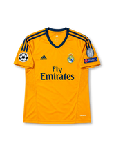 レアル・マドリード 2013/14シーズン サードユニフォーム ルカ・モドリッチ19番。adidas製の鮮やかなオレンジのボディに、ダークネイビーのVネック、肩のスリーストライプを組み合わせたレトロサッカージャージ。胸元にはダークネイビーのadidasロゴ、レアル・マドリードのクラブエンブレム、Fly Emiratesスポンサーロゴを配置。袖にはUEFAチャンピオンズリーグのスターボールパッチ、欧州9度制覇の記念パッチ、RESPECTパッチを備え、背面にはMODRIĆのネームと19番、襟下にはREAL MADRIDの文字を配したデザイン。