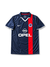 Paris Saint-Germain 2001-02 home jersey featuring Ronaldinho #21, Nike navy blue soccer shirt with an offset red vertical stripe, white V-neck detailing, OPEL sponsor logo, Nike Swoosh, PSG club crest, and RONALDINHO name and number 21 on the back of this retro soccer jersey.