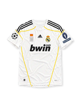 Real Madrid 2009-10 home jersey by adidas, featuring a classic white soccer shirt with navy three-stripe shoulder detailing, subtle gold piping, white crew neck collar, black bwin.com sponsor logo, adidas branding, Real Madrid club crest, and tonal Santiago Bernabeu-inspired graphics on the front.