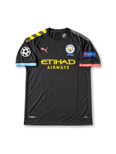 Manchester City 2019-20 away jersey featuring Nicolas Otamendi #30, black PUMA soccer shirt with yellow and black diagonal shoulder graphics, pink PUMA logo, yellow Etihad Airways sponsor branding, 125 Years Manchester City crest, contrasting sky blue and pink sleeve cuffs, UEFA Champions League sleeve patches, and OTAMENDI name with number 30 on the back.