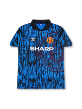 Manchester United 1992-94 third jersey featuring Eric Cantona #7, classic Umbro Newton Heath-inspired soccer shirt with a green and yellow half-and-half design, black lace-up polo collar, tonal geometric fabric pattern, black SHARP sponsor logo, Umbro branding, Manchester United club crest, and CANTONA name with black number 7 on the back.