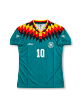 Germany 1994-96 away jersey featuring Lothar Matthaus #10, teal green adidas soccer shirt with striking black, red and yellow geometric diamond graphics across the shoulders and upper chest, German flag-colored V-neck collar, white adidas logo, German national team crest, front number 10, and MATTHÄUS name with white number 10 on the back.