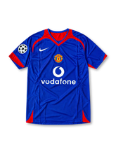 Front view of the 2005/06 Manchester United blue away soccer jersey by Nike, featuring red shoulder accents, a central club crest, white Vodafone sponsor, and UEFA Champions League sleeve patch.