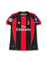 Front view of the 2010/11 AC Milan home soccer jersey featuring red and black vertical stripes, white adidas logo, Fly Emirates sponsor, club crest with gold star, UEFA Champions League starball patch, seven-time winners badge, and UEFA Respect patch.