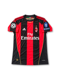 Front view of the 2010/11 AC Milan home soccer jersey featuring red and black vertical stripes, white adidas logo, Fly Emirates sponsor, club crest with gold star, UEFA Champions League starball patch, seven-time winners badge, and UEFA Respect patch.