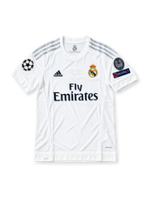 Front view of the Real Madrid 2015/16 white home soccer jersey featuring silver adidas shoulder stripes, dark navy Fly Emirates sponsor, crowned club crest, UEFA Champions League starball patch, 10-time European Cup winners badge, and UEFA Respect sleeve patch.