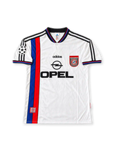 Front view of the Bayern Munich 1996-98 adidas away soccer jersey in white with vertical blue and red stripes, black polo collar, adidas Three Stripes, Opel chest sponsor, club crest, and UEFA Champions League sleeve patch.