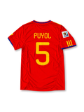 Front view of the Spain 2010 red home football jersey featuring Carles Puyol number 5, yellow Adidas shoulder stripes, blue neckline detailing and the Spanish national team crest.