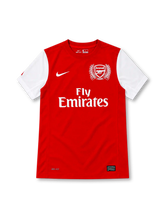 Arsenal 2011/12 red home jersey with white sleeves, white Nike Swoosh, Fly Emirates sponsor, and special 125th-anniversary laurel crest.