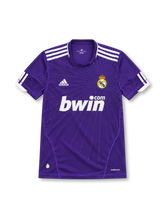 Real Madrid 2010/11 purple third jersey with subtle radiating starburst graphics, white adidas shoulder stripes, V-neck collar, crowned club crest, white bwin.com sponsor and ClimaCool branding.