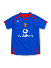 Manchester United 2005/06 royal-blue away jersey with red curved shoulder panels, red-trimmed V-neck collar, white Nike Swoosh, central club crest, white Vodafone sponsor and red side accents.