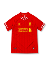 Liverpool 2013/14 red Warrior home jersey featuring subtle tonal pinstripes, white-trimmed V-shaped collar and sleeve cuffs, yellow Warrior logo, yellow Liver Bird crest and Standard Chartered sponsor.