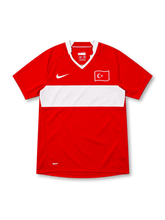 Türkiye 2008 red Nike home jersey featuring a wide white horizontal chest stripe, white-trimmed V-neck collar, white Nike Swoosh, Turkish crescent-and-star flag emblem, and NikeFIT branding.